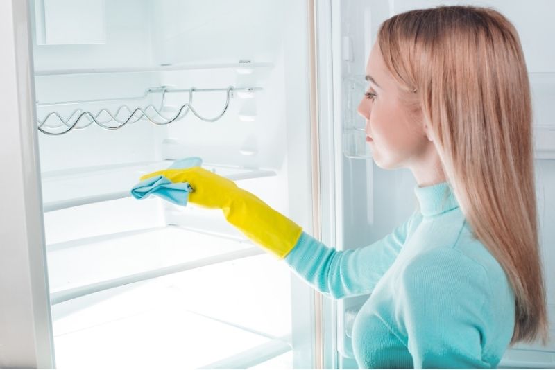 a girl wearing a yellow gloves doing a fridge cleaning