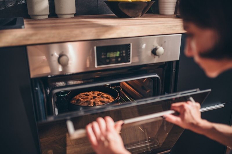 girl holding the oven door with a pan of bread inside