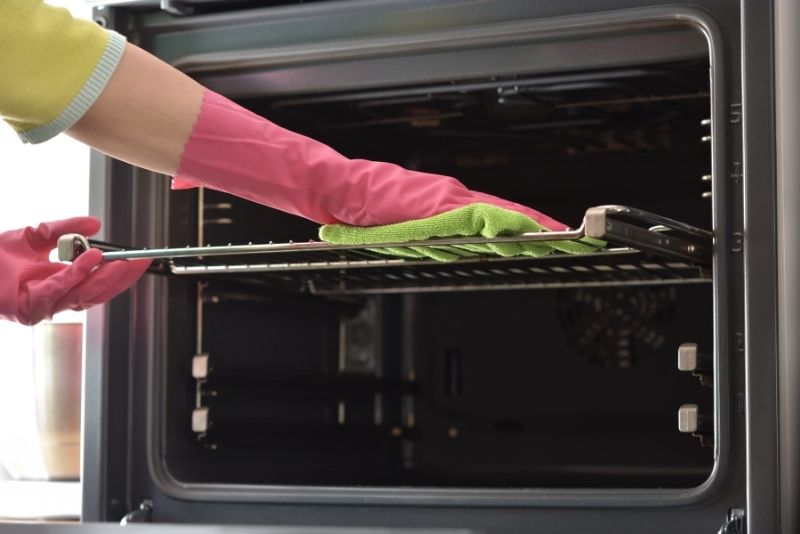 hands covered with pink gloves cdoing a oven cleaning
