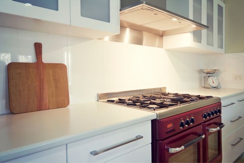 a picture of a kitchen with maroon oven and lighter rangehood